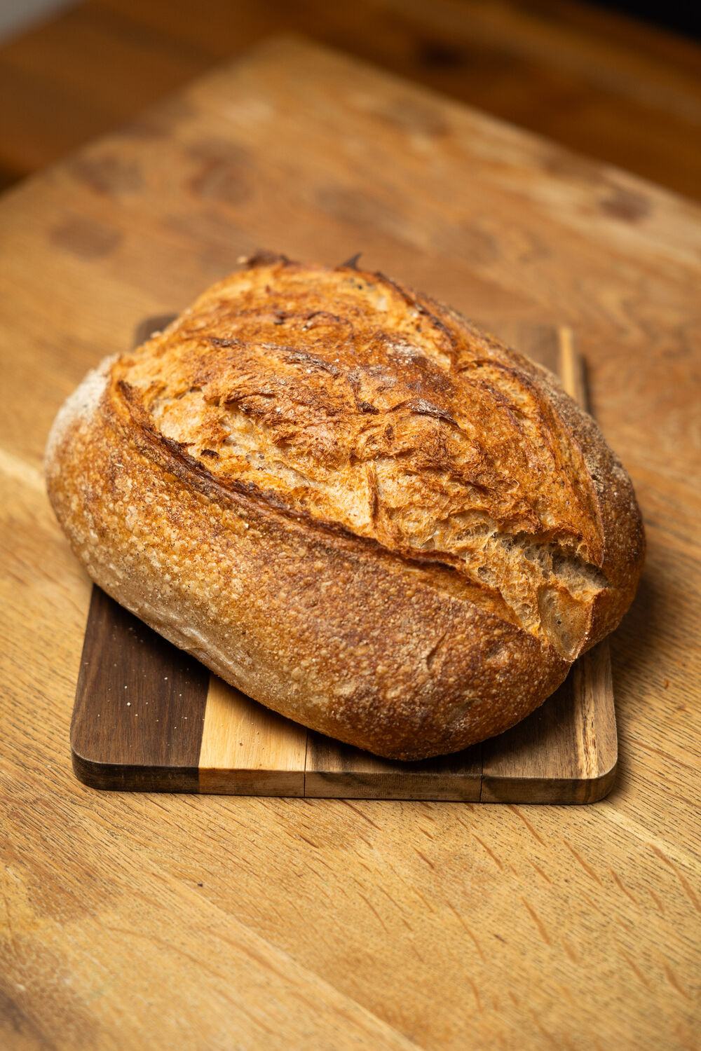A sourdough loaf with a dark, blistered crust on a wooden board.